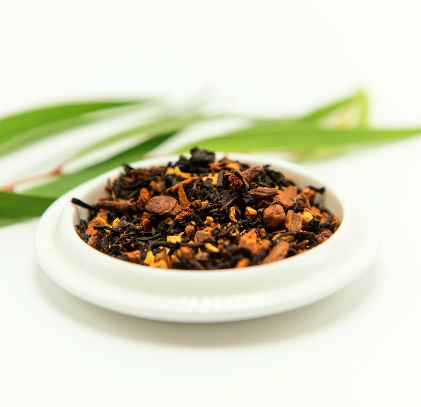 Coconut Chai Black Tea loose leaves in a white dish with greenery background.